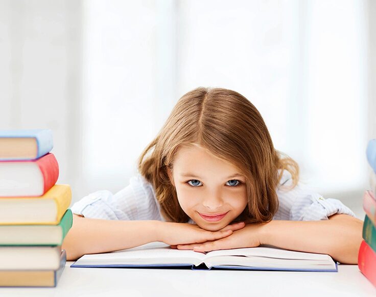 A girl is laying on the table with her head resting on an open book.